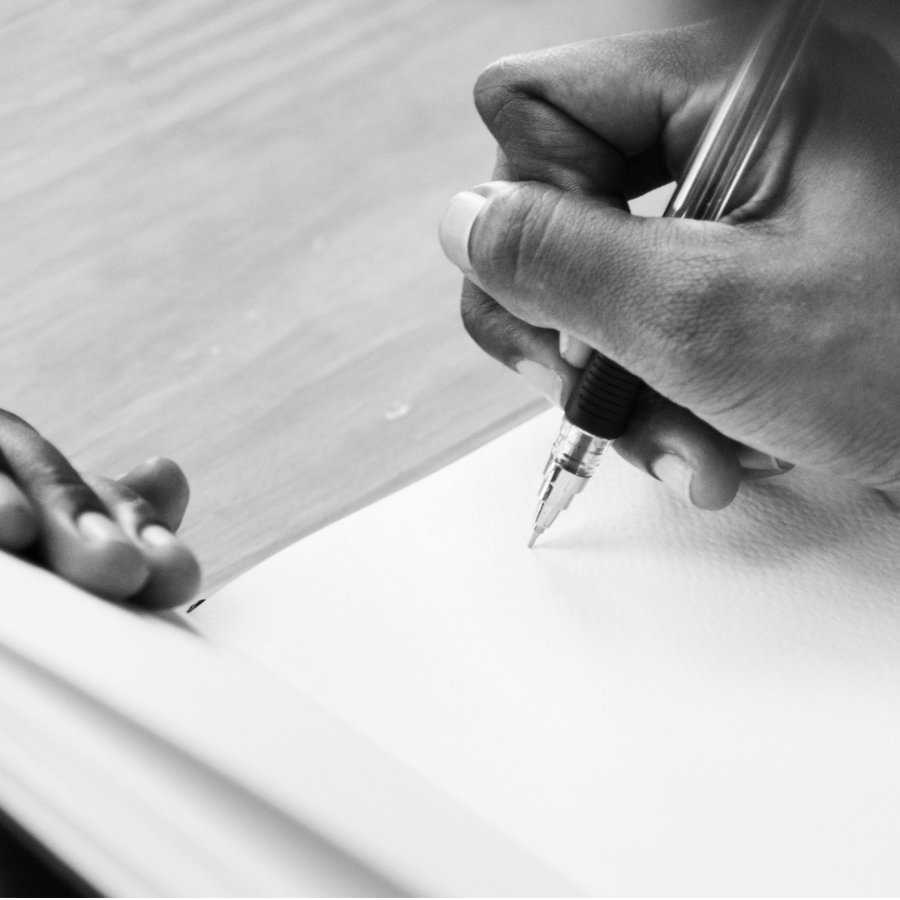 Eine Frauenhand, die einen Stift hält und in ein leeres Buch schreibt