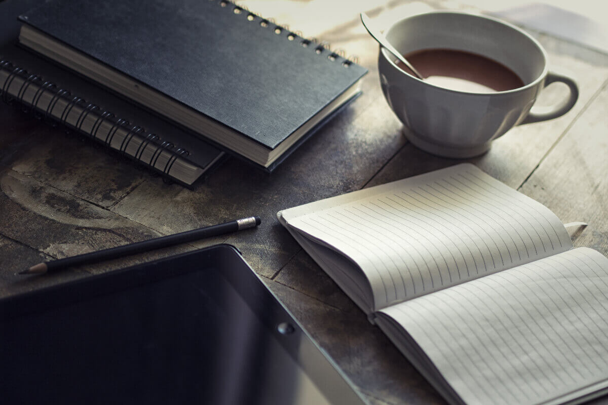 Ein aufgeschlagenes Notizbuch auf einem Tisch, daneben eine Tasse Kaffee; ein Tablet als Symbol für inneren Lärm.