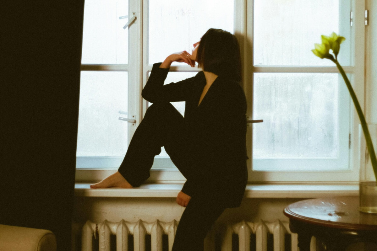 Frau blickt aus dem Fenster, während ihr Kopf voller Gedanken ist