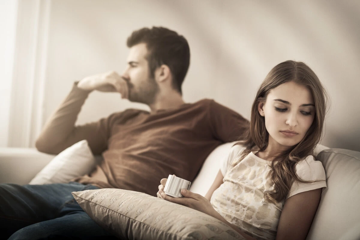 Wenn Nähe Angst macht Ein Paar sitzt schweigend nebeneinander auf einem Sofa und wirkt emotional voneinander entfernt.