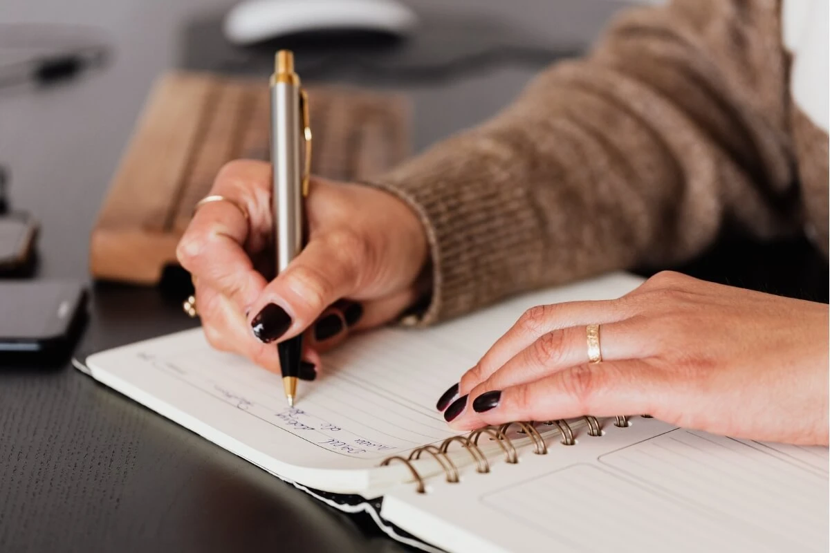 Schreiben bringt den Blick zurück zu dir Eine Frau schreibt mit Stift in ein Notizbuch.